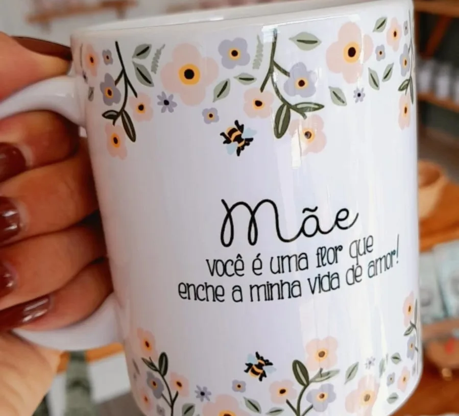 Foto da caneca tirada no celular, na mão, com a loja ao fundo